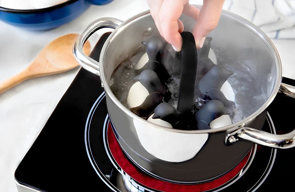 Egguins pinguïn eierhouder met eieren in een pan met kokend water op het fornuis