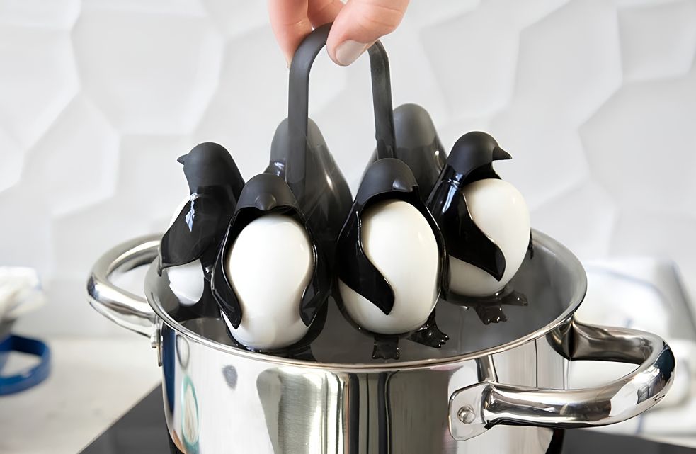 Hand tilt de Egguins eierhouder met zes pinguïns aan het handvat uit een roestvrijstalen pan