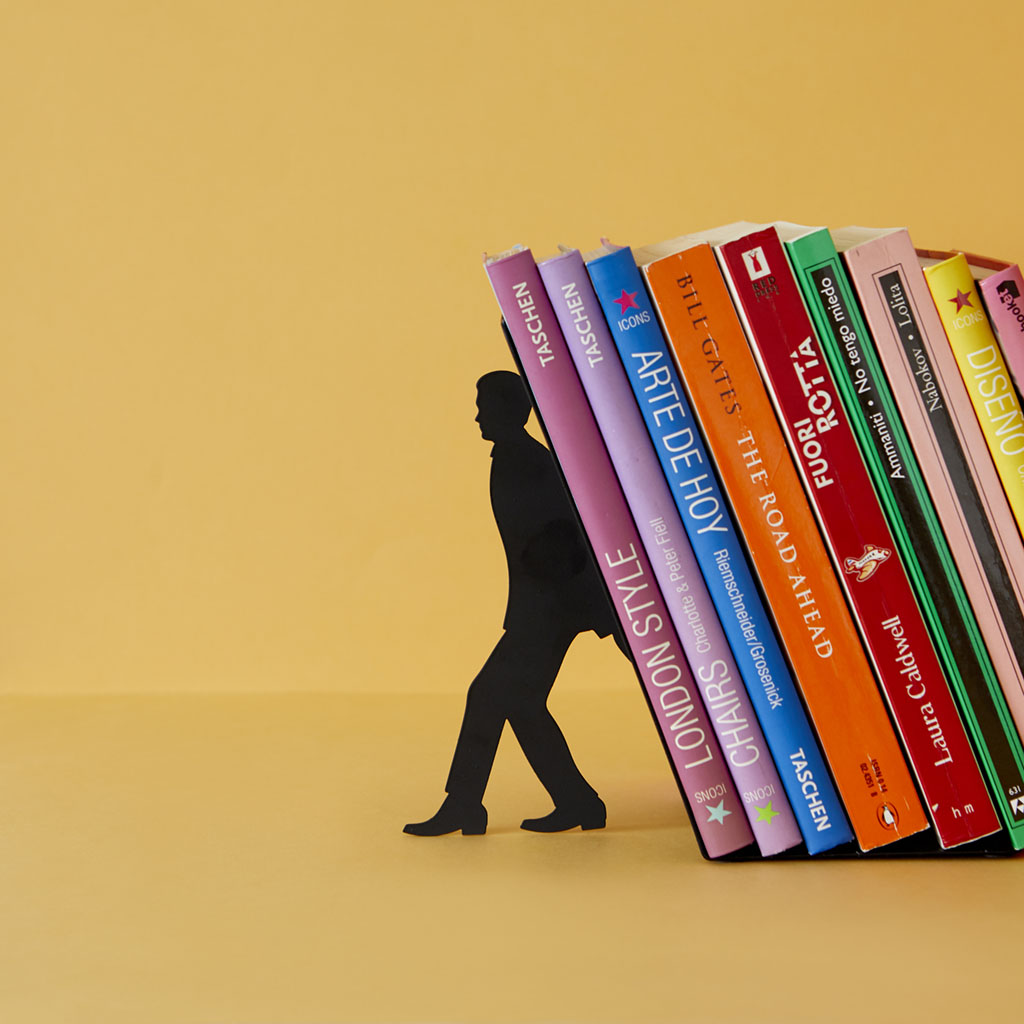Zwarte boekensteun in de vorm van een man die een schuine rij kleurrijke boeken ondersteunt tegen een gele achtergrond