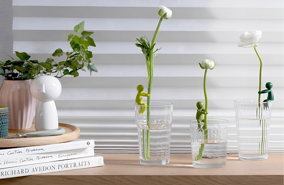Drie groene Leafriend plantenfiguurtjes ondersteunen witte bloemen in glazen met water