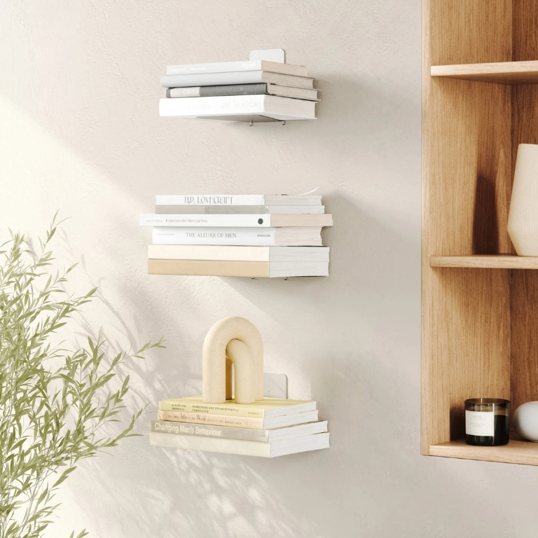 Drie zwevende boekenplanken van Umbra met stapels boeken aan een lichte muur in een modern interieur